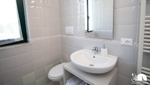 A bathroom with white tiles, a sink, a toilet, a mirror, and a window. - Luxury Martina Appartamenti-2-ortensia (Moniga del Garda)