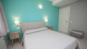 A bedroom with a bed, two bedside tables, a nightstand, a wall-mounted lamp, a door, and a laundry basket. - Luxury Martina Appartamenti-2-ortensia (Moniga del Garda)