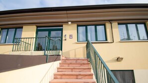 A building with a beige exterior, green window frames, and a staircase with a green railing leading to a door. - Luxury Martina Appartamenti-7-ibiscus (Moniga del Garda)
