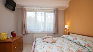 A bedroom with a bed, a nightstand, a lamp, a window with curtains, a radiator, and a television on the wall. - Luxury Martina Appartamenti-7-ibiscus (Moniga del Garda)