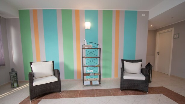 A hallway with two wicker chairs with white cushions, a metal shelf unit, and a striped wall. - Luxury Martina Appartamenti-7-ibiscus (Moniga del Garda)