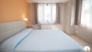 Habitación de hotel con cama, mesita de noche, ventana con cortinas y una lámpara fijada en la pared.