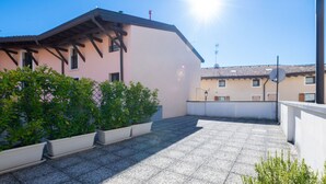 A rooftop terrace with potted plants, a building with a sloped roof, and a clear sky. - Appartamento Lilli in Manerba del Garda (Manerba del Garda)