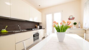 A modern kitchen with white cabinets, a central island, and a vase of tulips. - Appartamento Lilli in Manerba del Garda (Manerba del Garda)