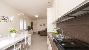 A compact kitchen with a dining area, a stove, and a bicycle decoration on the wall. - Appartamento Lilli in Manerba del Garda (Manerba del Garda)