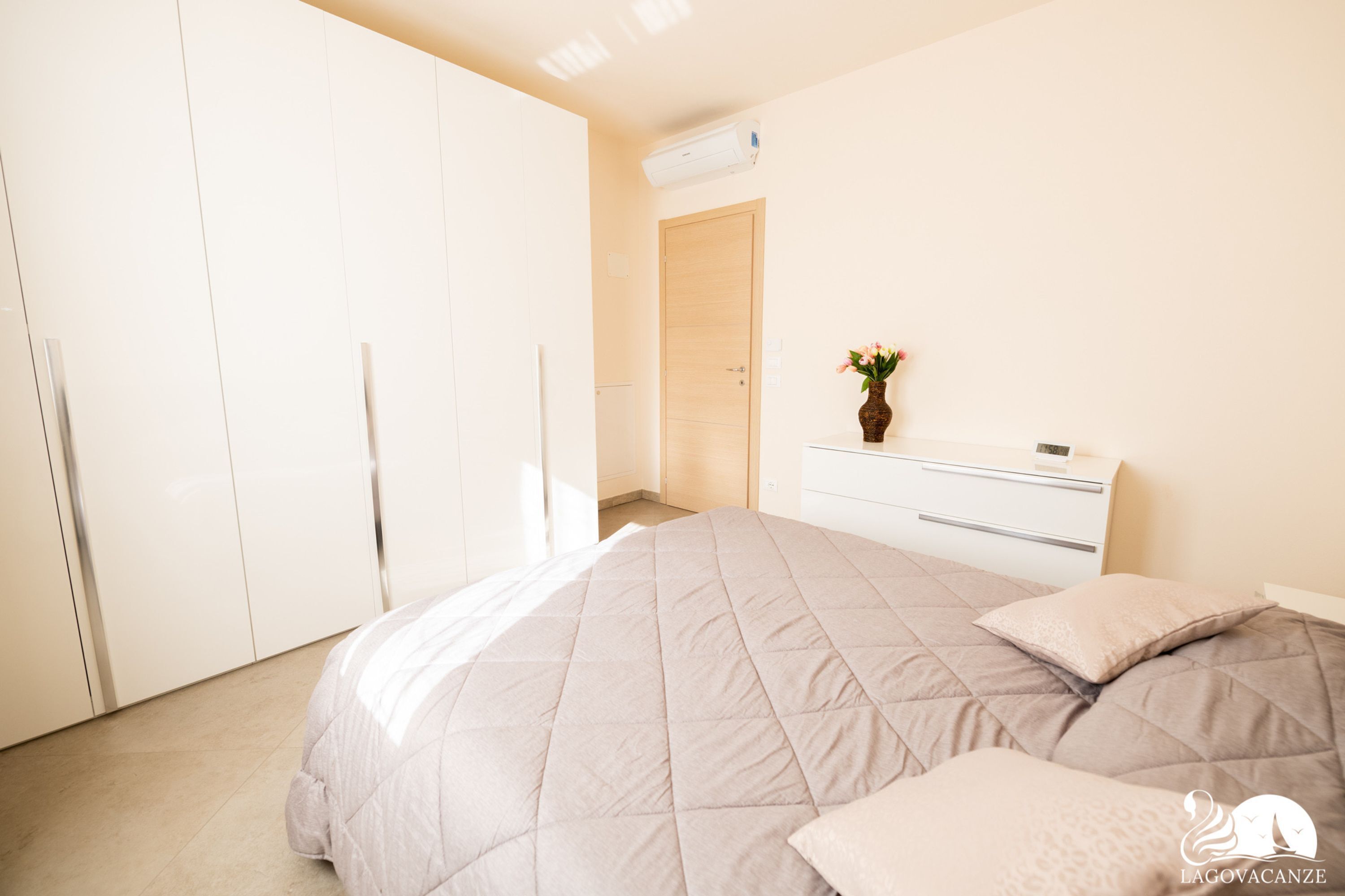 A bedroom with a bed, a dresser, a vase with flowers, and a door.