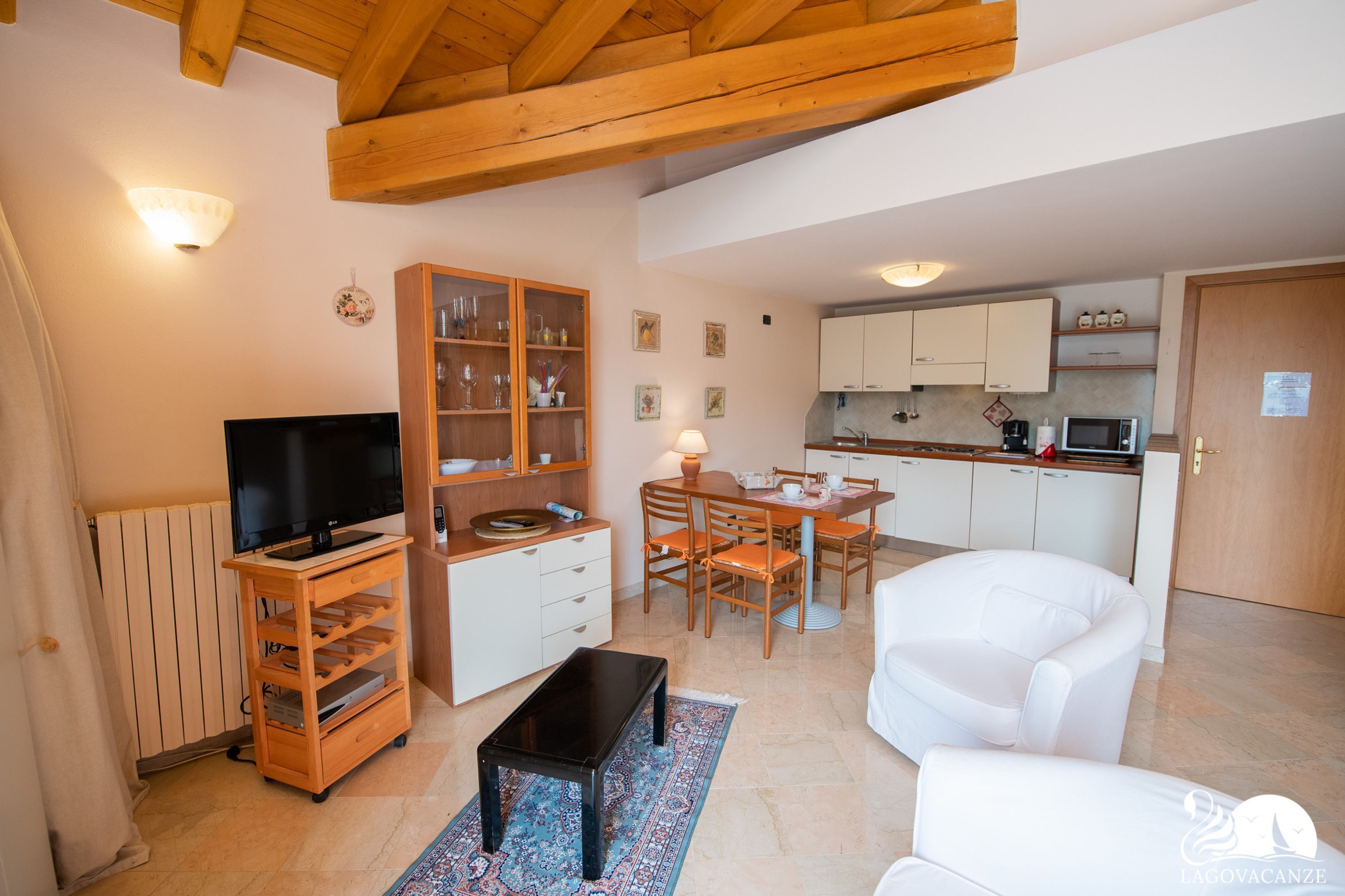 A compact living space with a TV, wooden entertainment unit, dining table, chairs, and a white sofa.