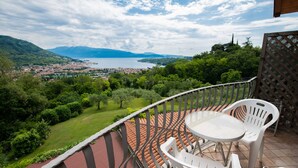 Un balcon avec vue sur un lac et des montagnes, des chaises en plastique blanches et un sol carrelé.