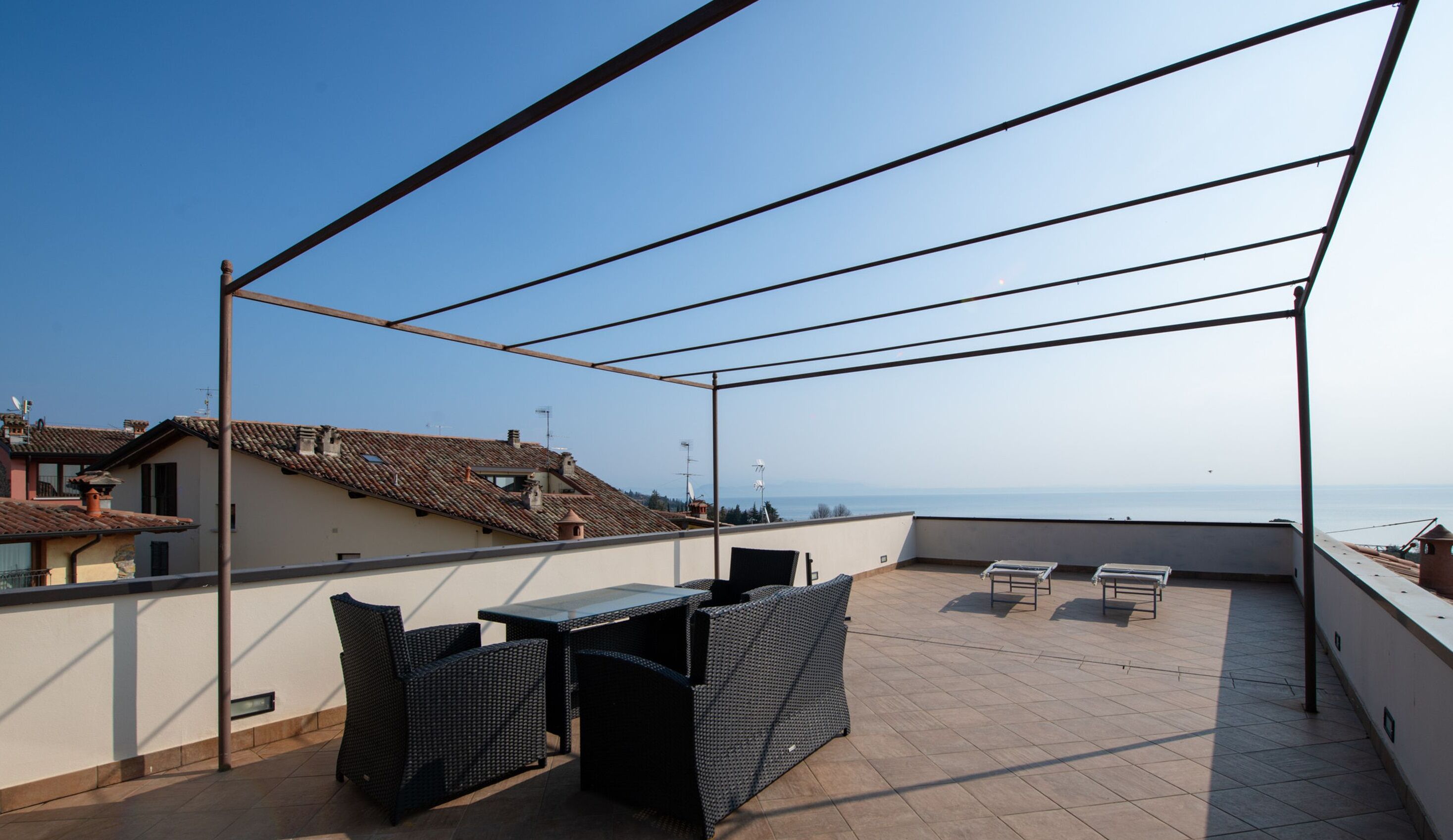A rooftop terrace with a table and chairs, overlooking a coastal view.