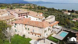 A stone building with a pool, surrounded by greenery and overlooking a lake. - Luxus Gardoncino - La Terrazza sul Lago (Manerba del Garda)