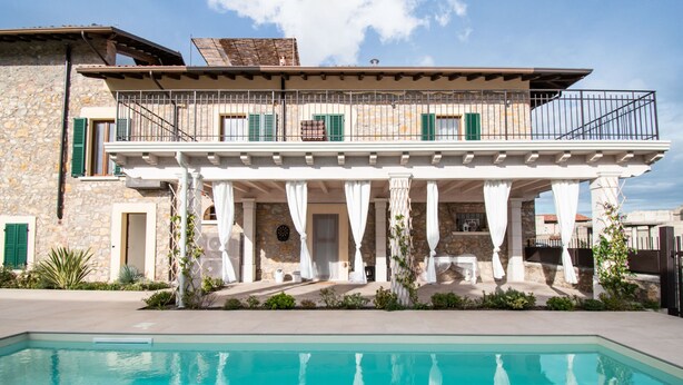 A two-story stone house with a balcony, a pool, and a covered outdoor seating area. - Luxus Gardoncino - La Terrazza sul Lago (Manerba del Garda)