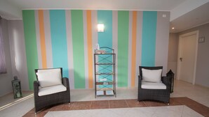 A hallway with two wicker chairs with white cushions, a metal shelf unit, and a striped wall. - Luxury Martina Appartamenti-3-fiordaliso (Moniga del Garda)