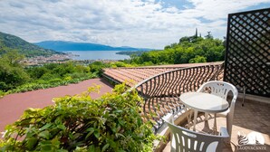 A balcony with a view of a lake and mountains, a red floor, and a white chair. - Feeling House - Appartamento Provenzale (Salò)