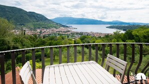 Eine Terrasse mit Tisch und Stühlen mit Blick auf eine Stadt und einen See, im Hintergrund Berge.