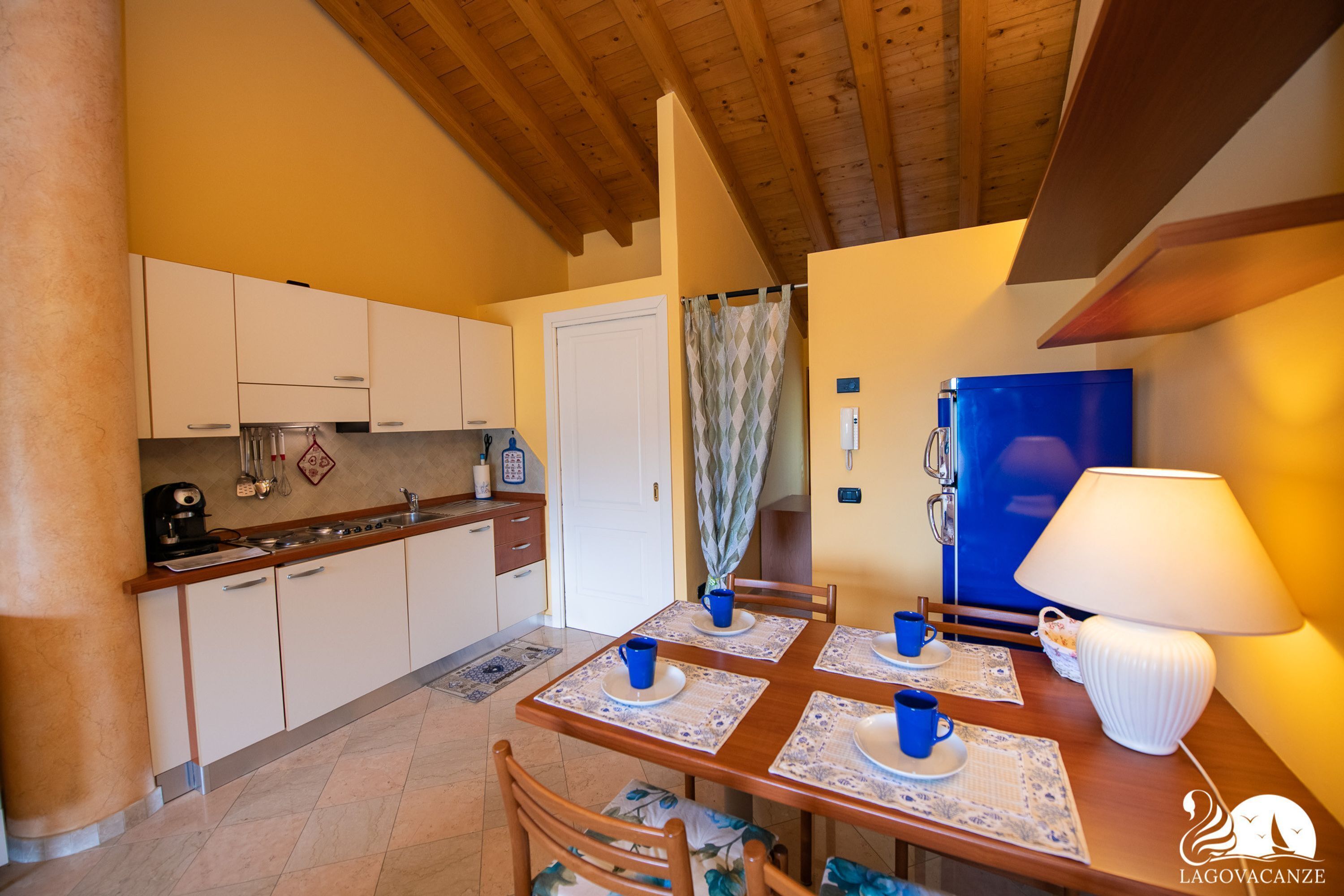 Una cocina acogedora con armarios de madera, una mesa de comedor con tazas y platos azules, y un refrigerador azul.