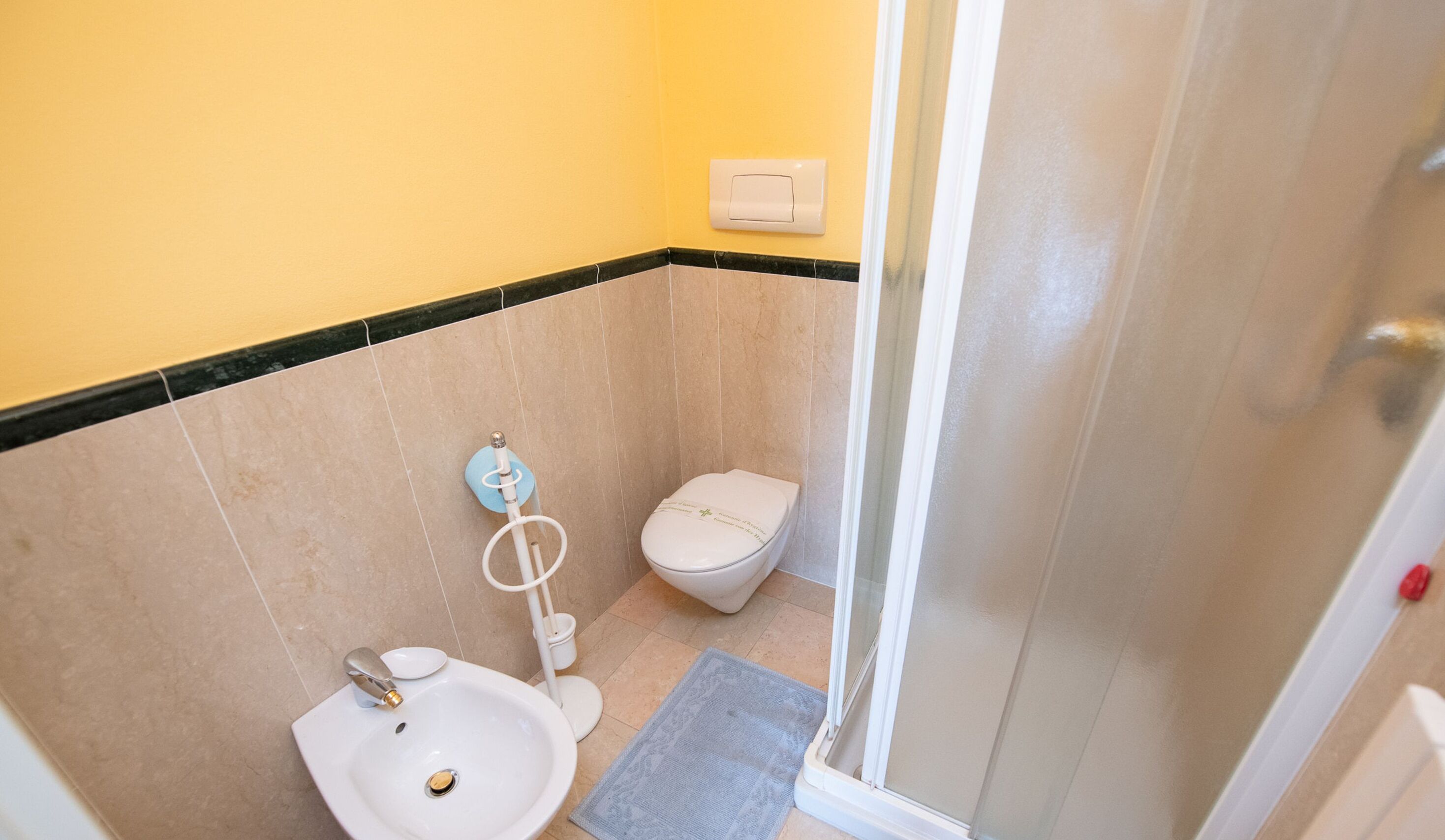 A small bathroom with a toilet, sink, and shower.