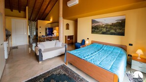 Ein Schlafzimmer mit einem hölzernen Bett, einer Couch, einem Schreibtisch und einem Stuhl. Ein Fenster bietet Blick auf eine Landschaft.