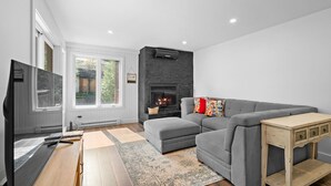 Ein modernes Wohnzimmer mit einem grauen Ecksofa, einem Flachbildfernseher, einem Kamin und einem Holztisch.