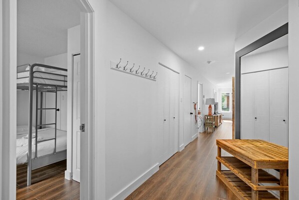 A hallway with a bunk bed, coat hooks, a wooden bench, and a door leading to another room.