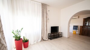 Una sala de estar con un televisor sobre un mueble bajo, una planta y un letrero que dice 'Welcome Have a Nice Day'.