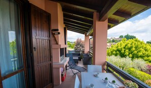 Un patio techado al aire libre con una mesa dispuesta para dos, una puerta de madera y vistas a un jardín y edificios a lo lejos.