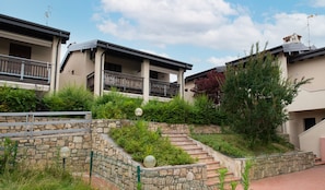 Una zona residencial con una escalera de piedra que lleva a un balcón, rodeada de vegetación y un muro de piedra.