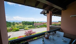 Un balcón con una mesa lista para el té, con vistas a un jardín ajardinado y edificios a lo lejos.