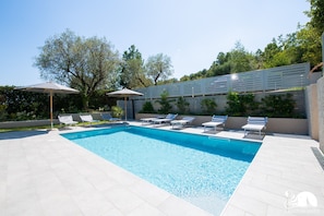 A rectangular swimming pool with clear blue water, surrounded by white tiled flooring. There are several white lounge chairs and umbrellas arranged around the pool. - L Agrumeto - Il Limone (Manerba del Garda)