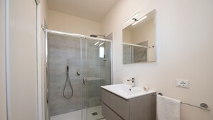 Un baño moderno con ducha de vidrio, un lavamanos blanco y un espejo sobre el mueble de tocador.