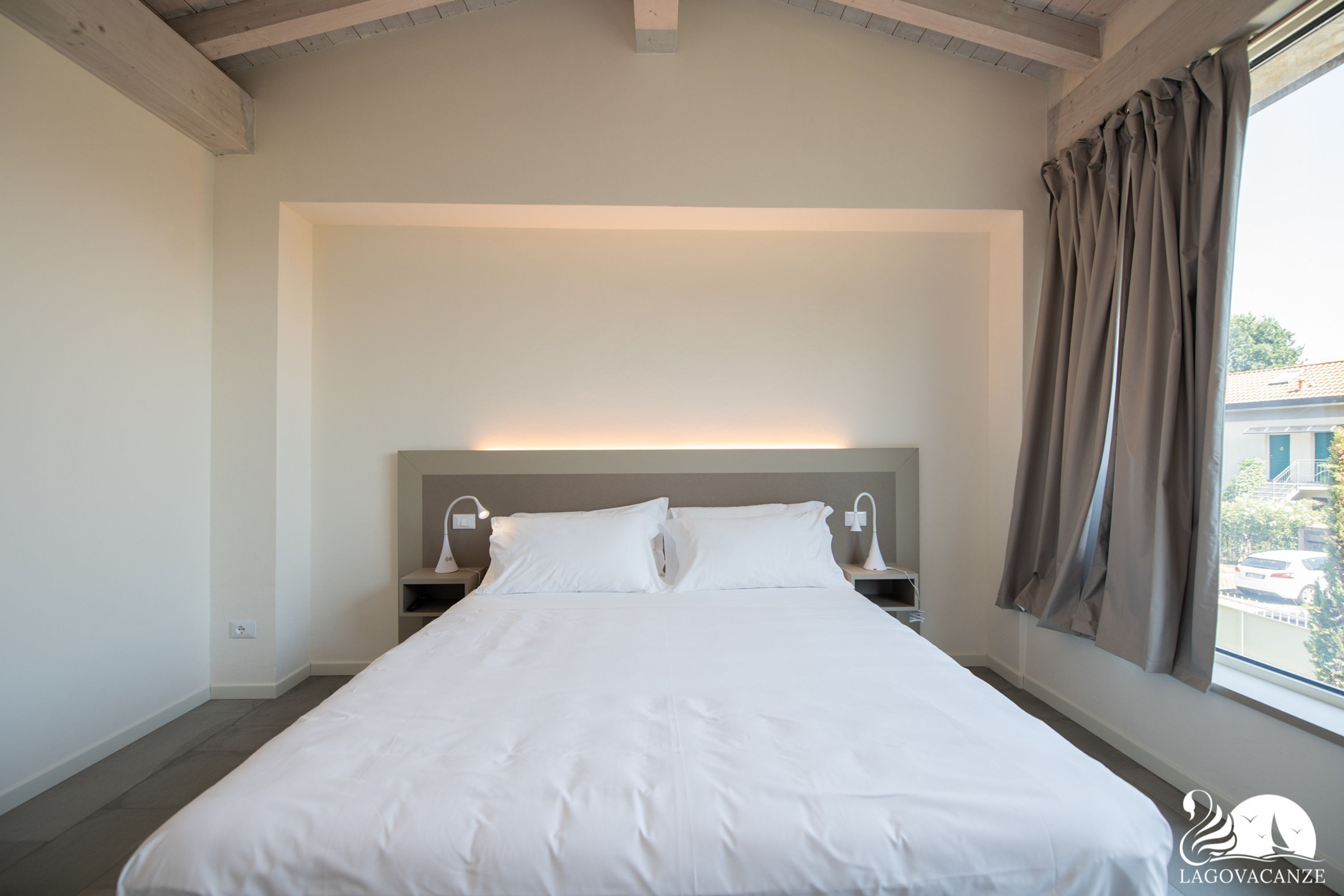 Habitación de hotel con una cama grande, lámparas de noche, una mesita de noche y una ventana con cortinas.