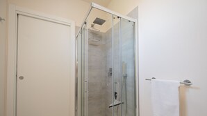 Une douche fermée par des parois de verre, avec une serviette blanche suspendue à un porte-serviettes.