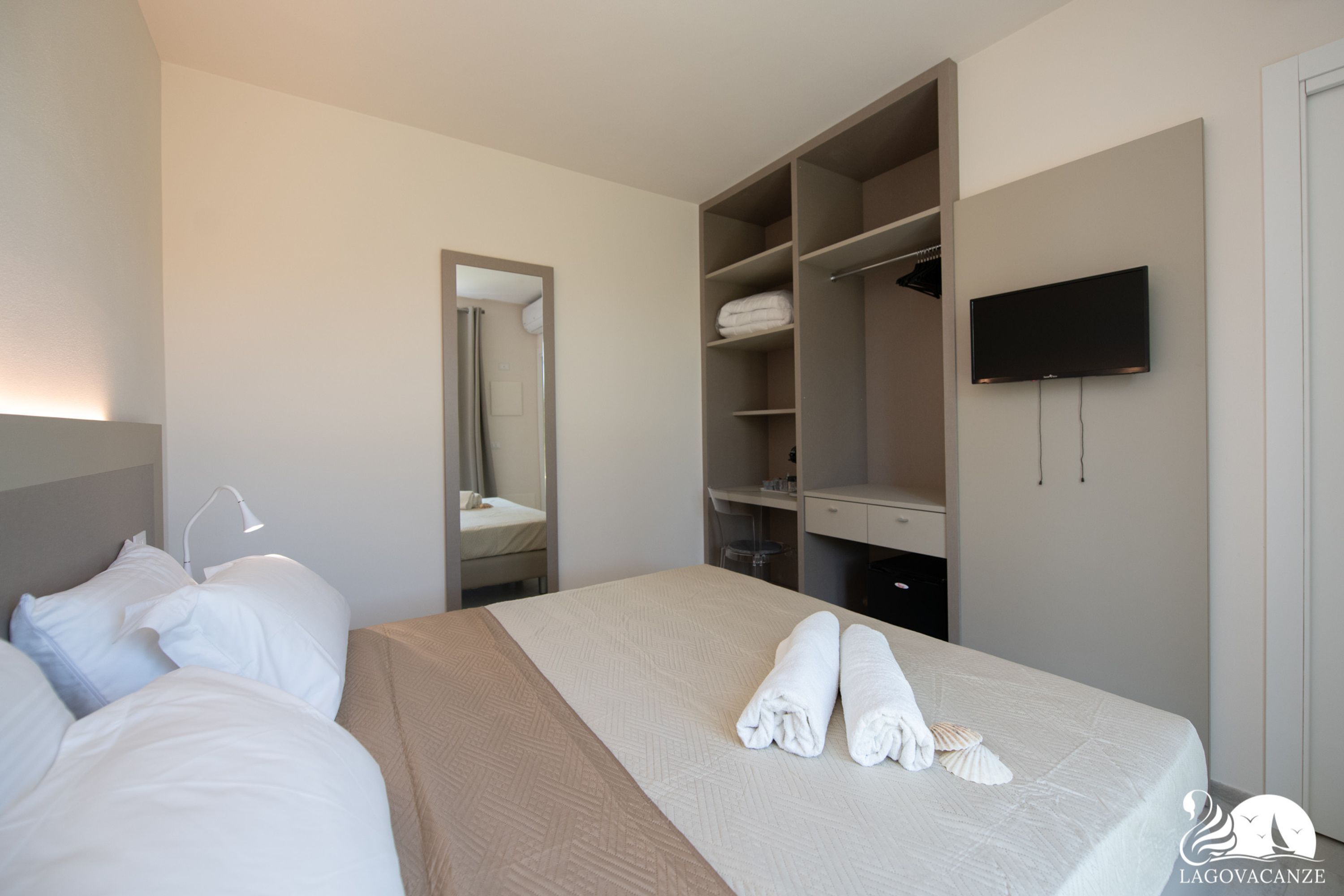 A hotel room with a bed, a wardrobe, a mirror, and a TV.