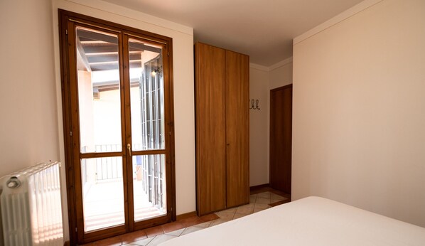 Un dormitorio con un amplio ventanal corredero que da a un balcón, un armario de madera y un radiador en la pared.