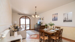 A dining area with a wooden table set for four, a chandelier, and artwork depicting New York and the Eiffel Tower. - Appartamento Katy in Polpenazze del Garda (Polpenazze del Garda)