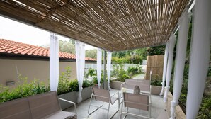 A covered patio area with white columns, cushioned seating, and a view of a garden with a red-tiled roof in the background. - L Agrumeto - L Arancia (Manerba del Garda)