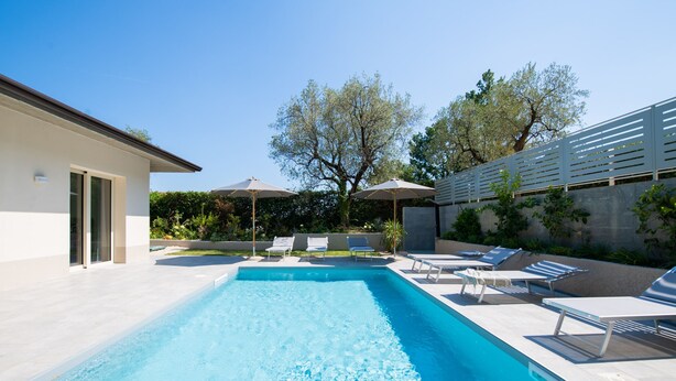 A swimming pool with lounge chairs and umbrellas, surrounded by a landscaped garden and a building. - L Agrumeto - L Arancia (Manerba del Garda)