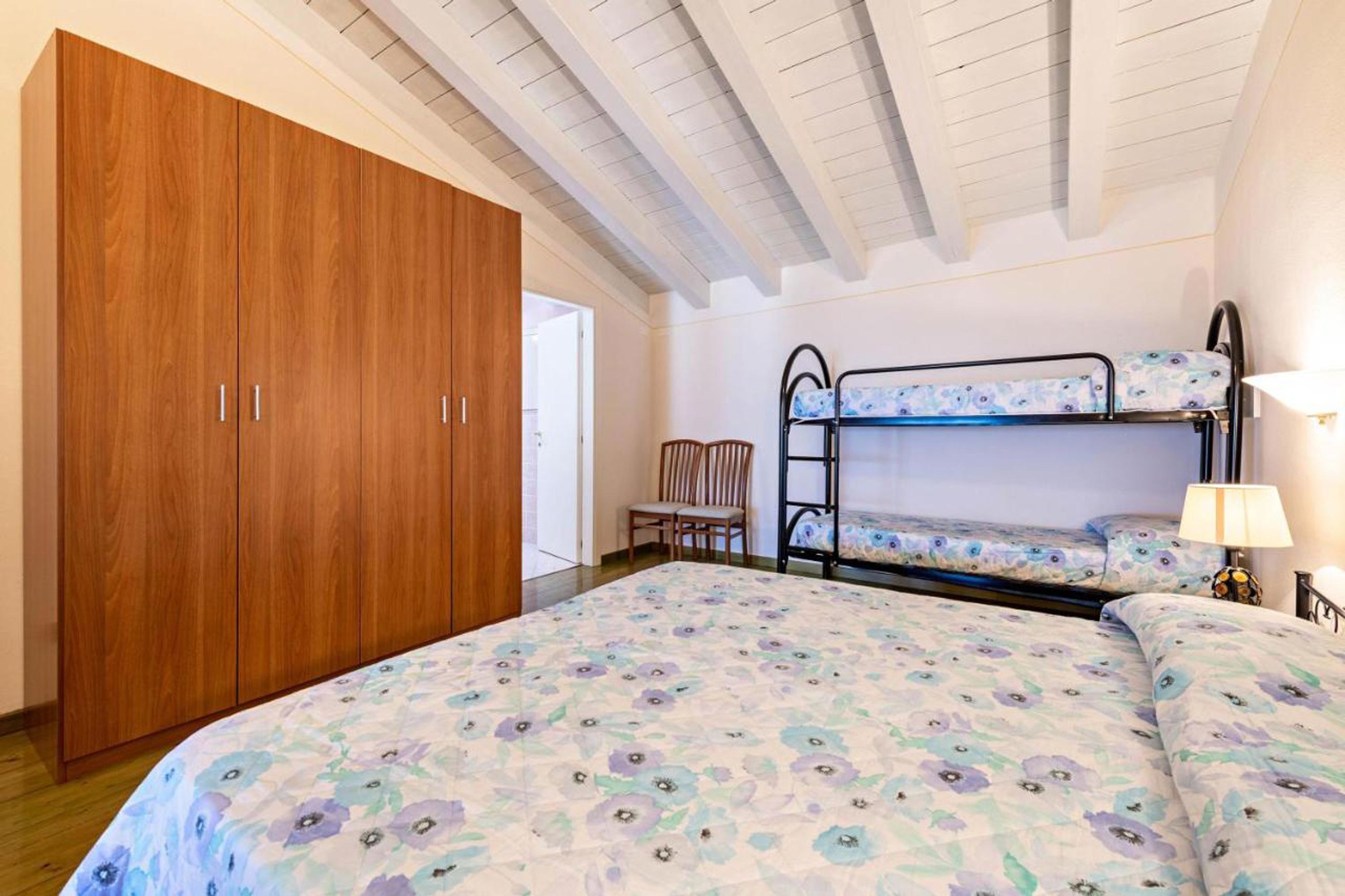 A bedroom with a bunk bed, wooden wardrobe, and a chair.
