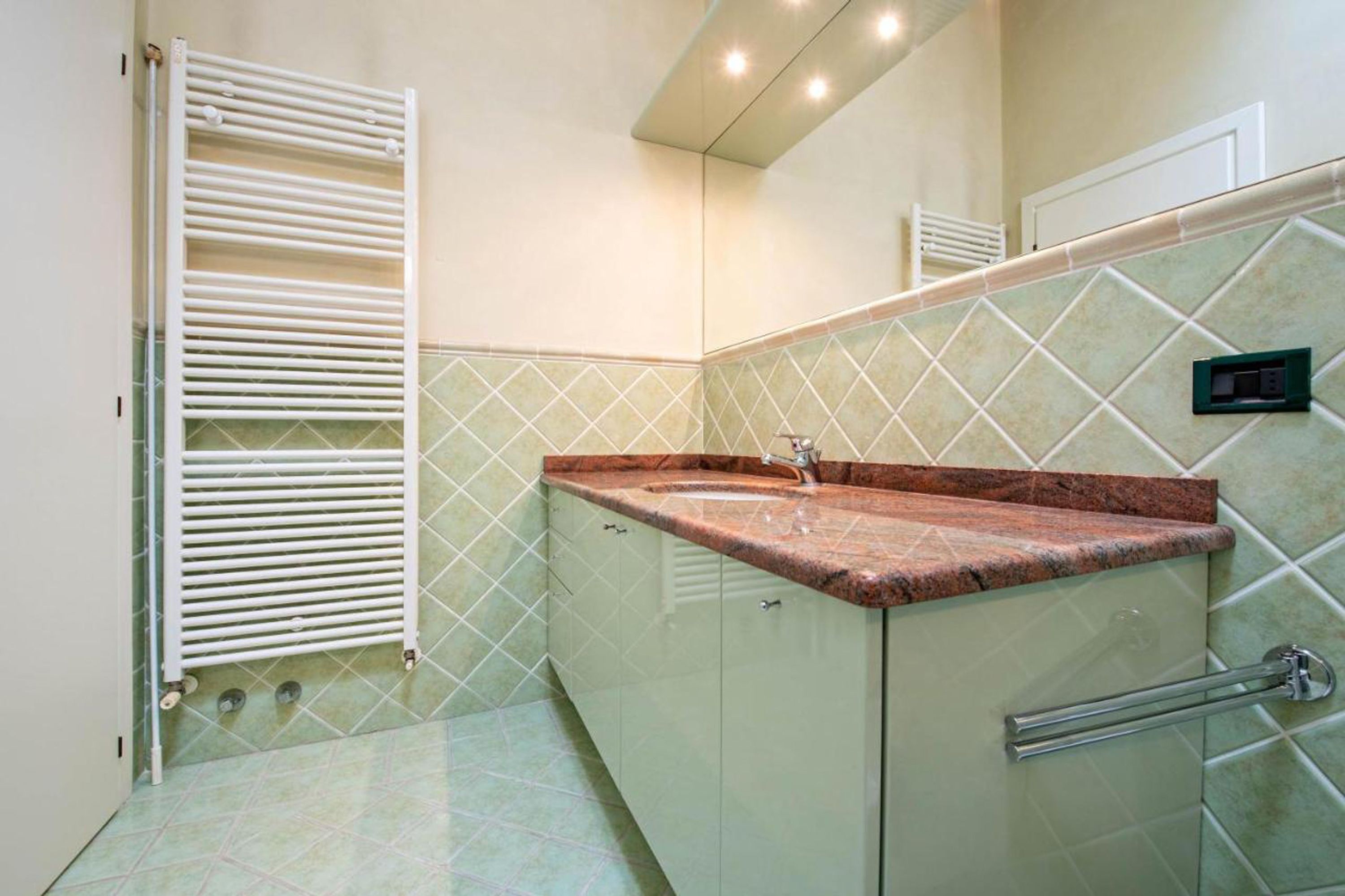 Une salle de bain avec un radiateur blanc, un lavabo doté d’un plan de toilette en marbre et un mur recouvert de carreaux.