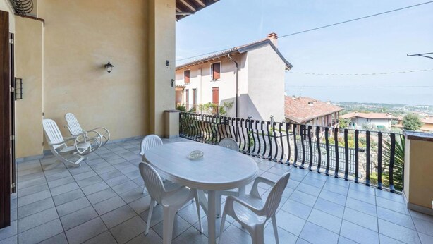 A balcony with a round table and four chairs, a metal railing, and a view of a residential area. - Casa Vacanze Baccolo - Appartamento Lucia (Polpenazze del Garda)