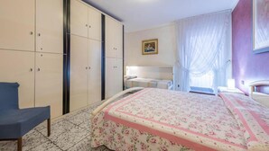A bedroom with a bed, a chair, a wardrobe, and a bedside table. - Casa Vacanze Baccolo - Appartamento Lucia (Polpenazze del Garda)