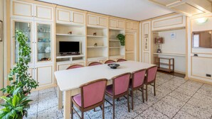 A dining area with a white table and pink chairs, surrounded by light-colored cabinets with glass doors. - Casa Vacanze Baccolo - Appartamento Lucia (Polpenazze del Garda)