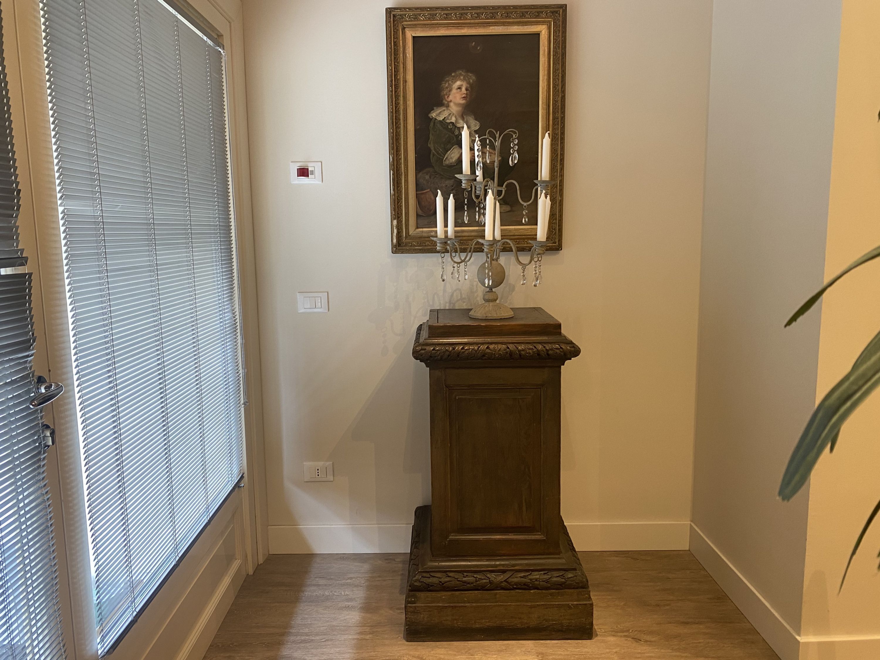 A hallway with a wooden pedestal, a framed painting, and a candelabra with candles.
