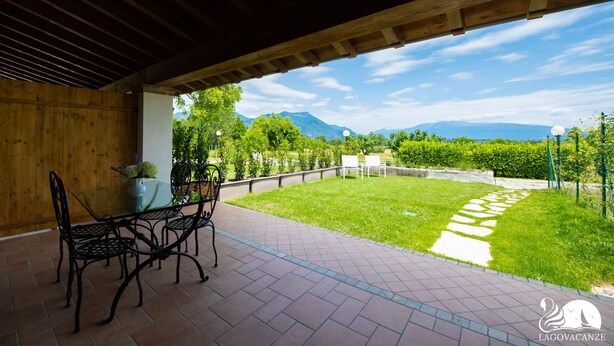 Un patio al aire libre con una mesa y sillas, un camino pavimentado y vistas a montañas y vegetación.