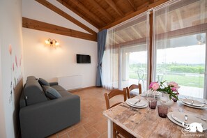 Un comedor con una mesa de madera para cuatro personas, un sofá gris y un televisor fijado en la pared.