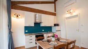 Cocina moderna con armarios blancos, salpicadero azul y vigas de madera. Hay una mesa de comedor con platos, vasos y un jarrón con flores.