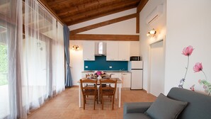Una cocina moderna con armarios blancos y un protector contra salpicaduras azul, un comedor con mesa y sillas, y una sala de estar con sofá y una pared decorada con motivos florales.