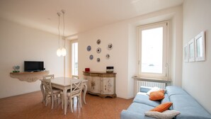 A dining area with a table and chairs, a television on a shelf, a cabinet with decorative plates, and a blue sofa with pillows.