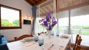 Un comedor con una mesa dispuesta para cuatro, un florero con flores moradas y vista a zonas verdes al exterior.