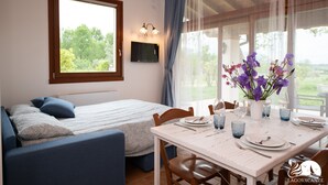 Una habitación con cama, una mesa de comedor preparada para dos personas y un ventanal con cortinas.