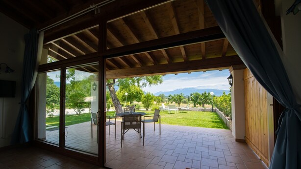 Una habitación con un amplio ventanal corredera que da a un patio exterior con una mesa y sillas, vista a un paisaje verde y techo de madera.